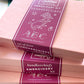 A stack of pink boxes with plum-colored belly bands that read "Sublime Stitching Embroidery Kit: Handkerchiefs"